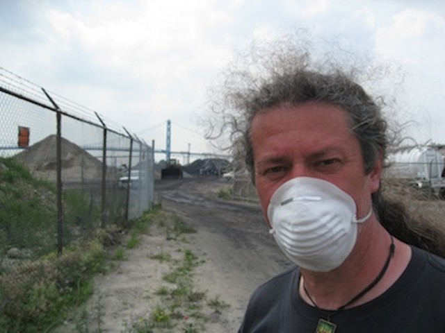 A protester stands in front of the piles of petcoke that graced the riverfront in 2013. The piles have since been removed.