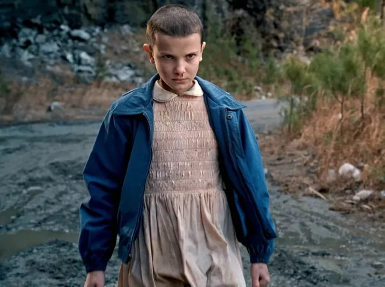 To be Eleven (aka the best Stranger Things character) you need a Short Blonde wig, a pink ruffed dress with a white collar, a navy bomber jacket, a box of Eggo's, knee high white striped socks, and white sneakers. Photo courtesy of Netflix 