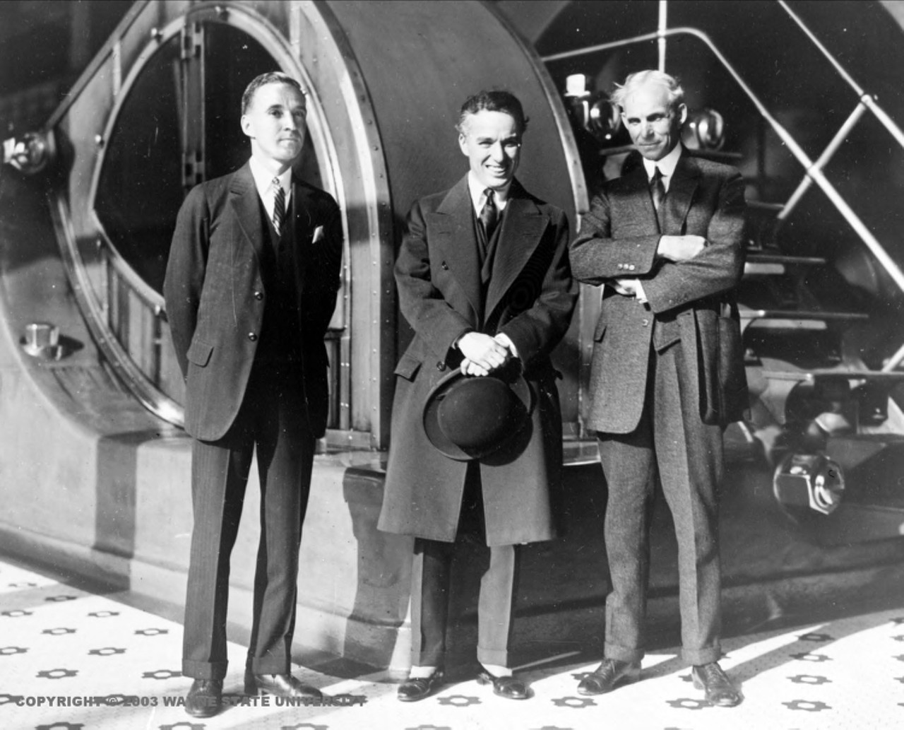 Portrait of Edsel Ford, Charles Chaplin and Henry Ford standing in front of a large piece of machinery. (Photo credit: Detroit News Collection, Walter P. Reuther Library, Wayne State University)