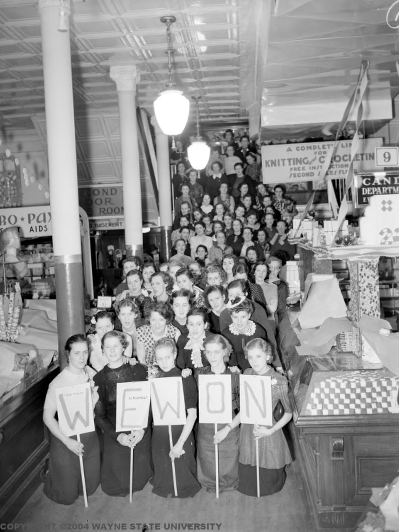 1930s | Large group of female employees pose for camera with signs that read, "We won," at conclusion of sit-down strike at Woolworth Company in Detroit, Michigan.