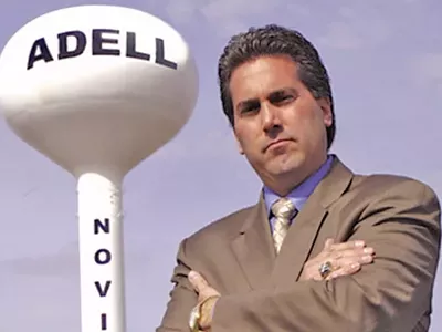 Kevin Adell posing next to a water tower bearing his name at the site of the contested property in Novi.