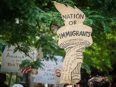 An activist in Detroit holds a protest sign shaped like the liberty torch that says “Nation of Immigrants.”