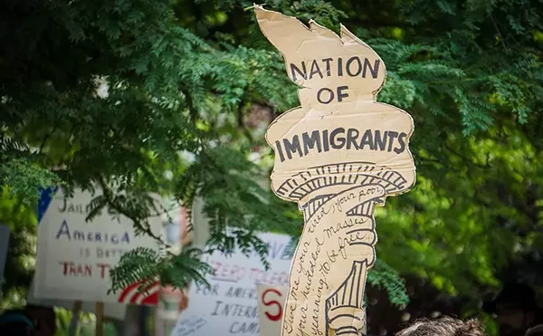 An activist in Detroit holds a protest sign shaped like the liberty torch that says “Nation of Immigrants.”