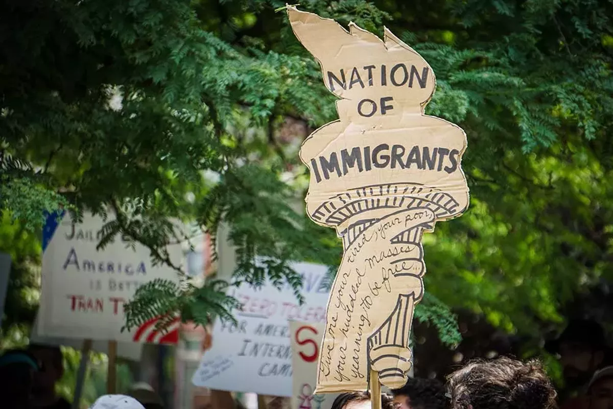 Image: An activist in Detroit holds a protest sign shaped like the liberty torch that says “Nation of Immigrants.”