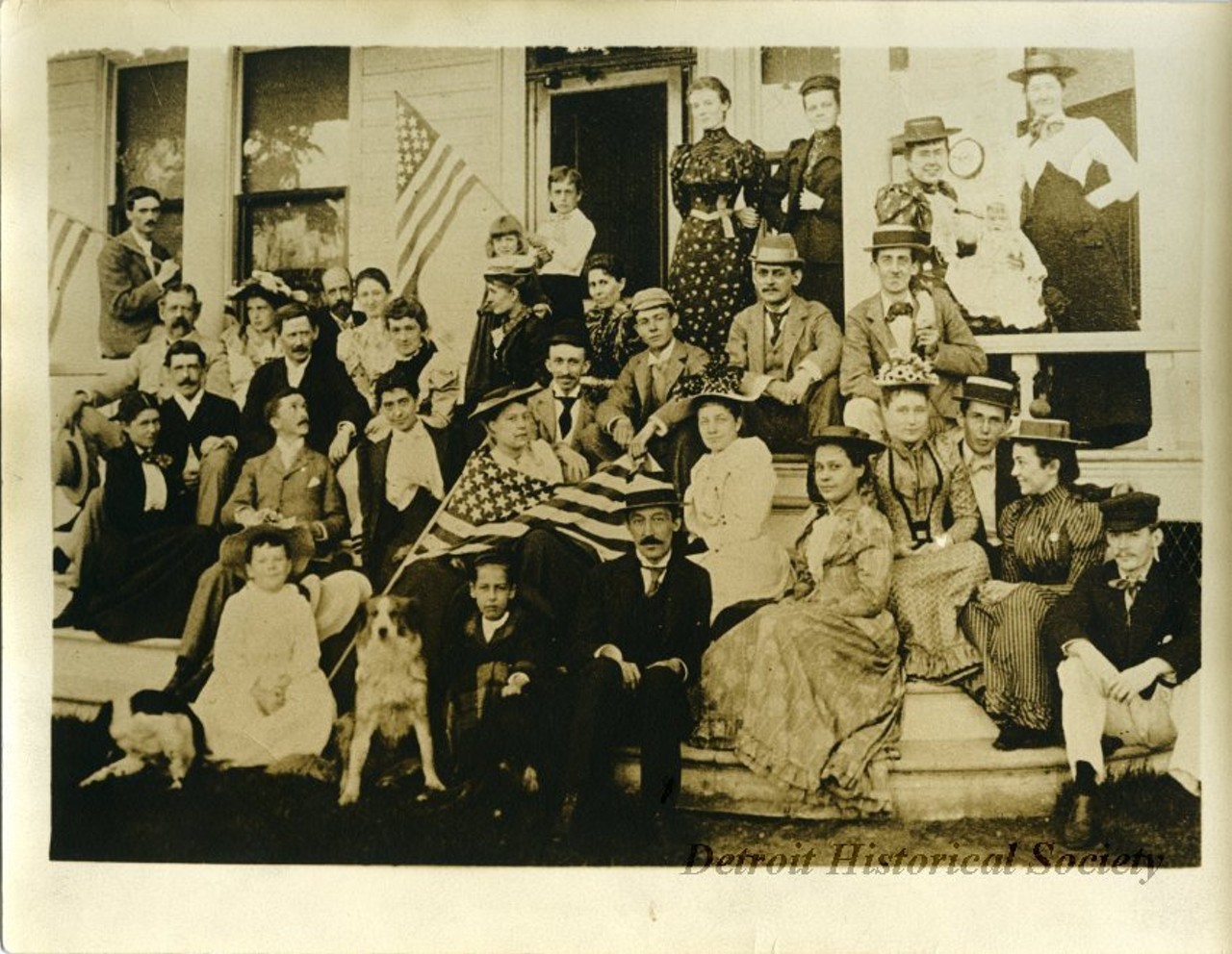 "Sepia-toned group photograph taken of people sitting and standing on the porch of the home of Mr. and Mrs. George H. Russel in Grosse Pointe for a Fourth of July celebration. Several people are holding American flags. On the verso is a handwritten description "Picture taken July 4, 1891 on porch of house of Mr. & Mrs. George H. Russel, Grosse Pointe," along with the names of the people in the photograph: "Mr. & Mrs. E. A. Sumner, Charles B. King, Alice King, Madeline King, Bessie Wright, Mr. & Mrs. W. K. Anderson, Mr. & Mrs. John R. Russel, Miss Sarah Russel, Miss Anne D. Russel, Edward A. Sumner Jr., Anna Sumner, Mrs. James J. Shaw, George B. Russel, Albert Russel, Sallie Russel, Philip Russel, Raymond Russel, Catherine Russel, Francis Russel, Marian Russel, James A. Venable, Anne Anderson, Pally Anderson, Sue Anderson, Louis B. Wright, Catherine Clark Anderson, Bessie Venable, Walter Brandon, Mr. & Mrs. George H. Russel, George L. Courtney.""
