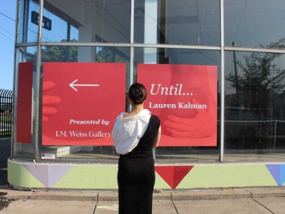 I.M. Weiss Gallery director Isabelle Weiss stands in front of a wayfinding sign for her latest exhibition in Stanton Yards.