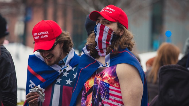 Two Trump supporters sporting MAGA hats, draped in Trump flags.