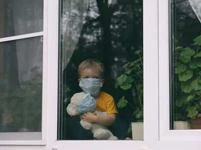 Sad child in protective medical masks looks out the window.