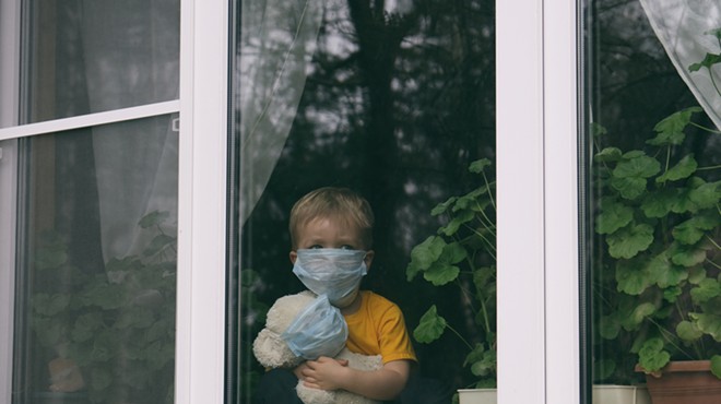 Sad child in protective medical masks looks out the window.