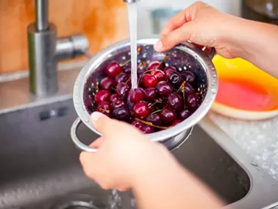 A woman washing cherries under a faucet.