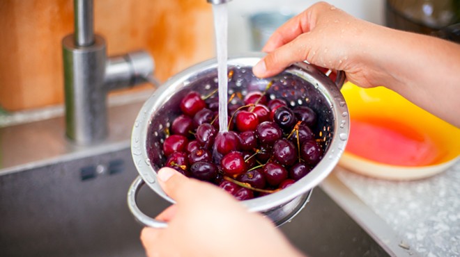 A woman washing cherries under a faucet.