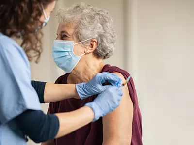 Doctor giving injection to senior woman at hospital.