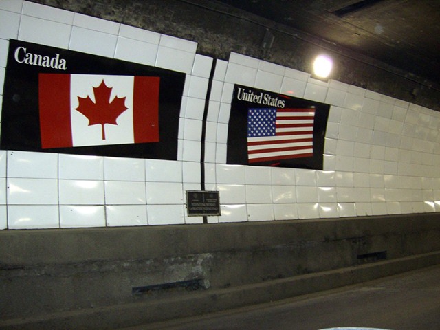 Flags of Canada and the United States over a metal boundary marker in the Detroit-Windsor Tunnel.