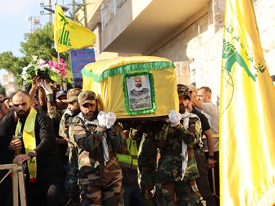 Hezbollah fighters, dressed in military uniform in Lebanon, carry a coffin wrapped in a yellow flag, mourning a fallen comrade from battles with Israel.