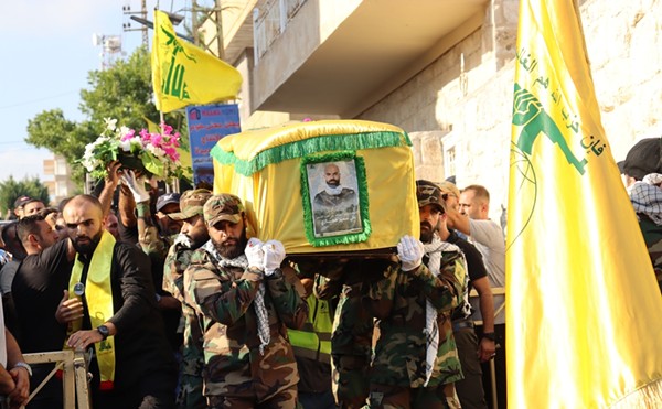 Hezbollah fighters, dressed in military uniform in Lebanon, carry a coffin wrapped in a yellow flag, mourning a fallen comrade from battles with Israel.