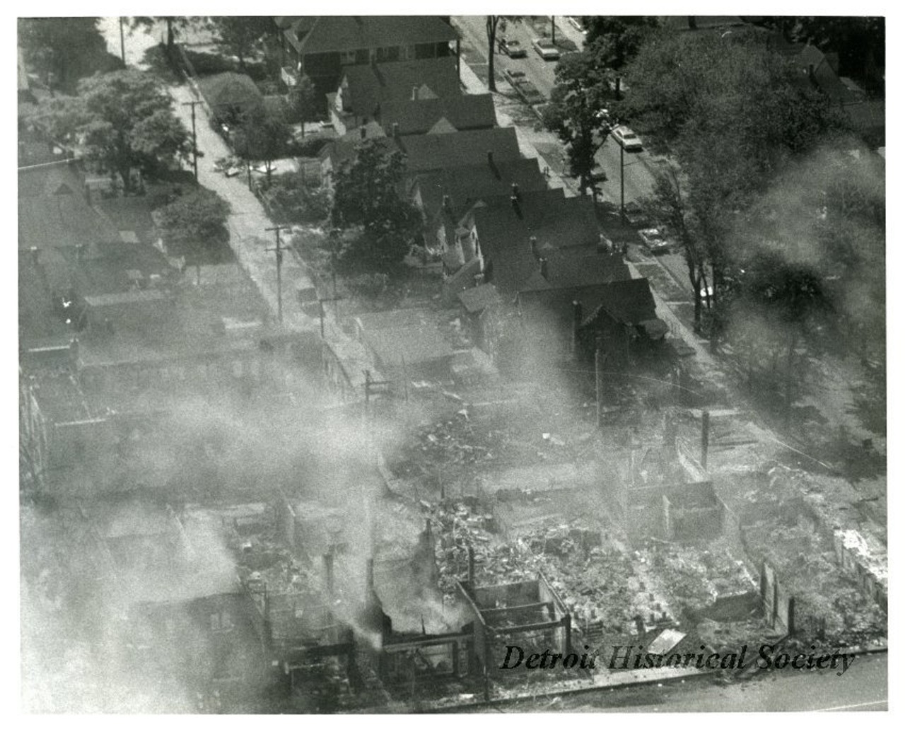 "One black and white aerial photograph of ruined buildings taken during the 1967 Detroit Riot. The photo shows the smoldering ruins of several blocks of houses and businesses that have been destroyed by fire."