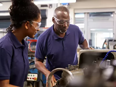 An engineer showing a teenage apprentice how to use a lathe.