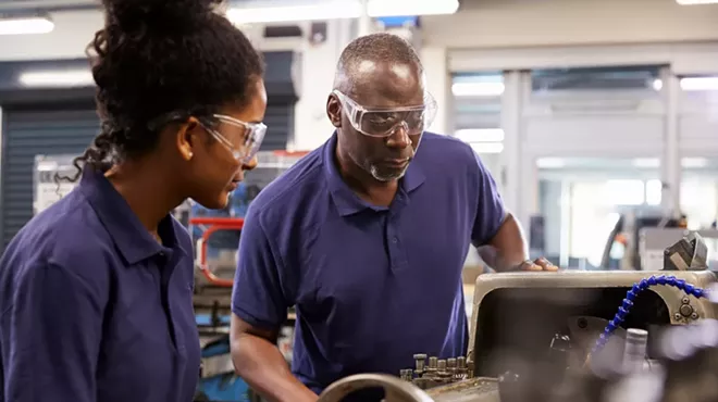 An engineer showing a teenage apprentice how to use a lathe.