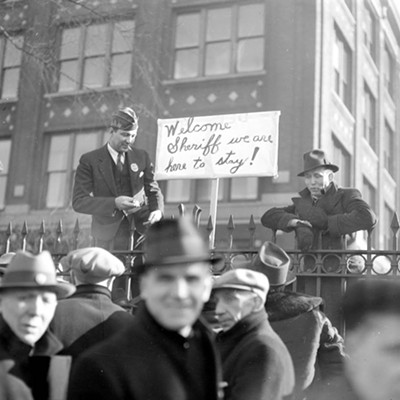 March 17, 1937: Men gather outside the Dodge plant in Detroit during a sit-down strike. One man stands next to a picket sign that reads, "Welcome Sheriff, we are here to stay!"