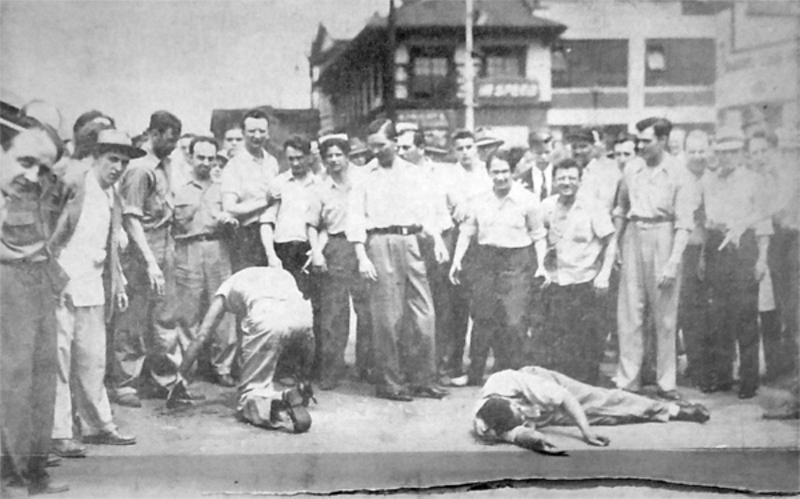White rioters swagger over their black victims in front of a gas station at Erskine and Woodward in this newspaper photograph. - Unidentified clipping, 1943 riot folder, Burton Collection, Detroit Public Library