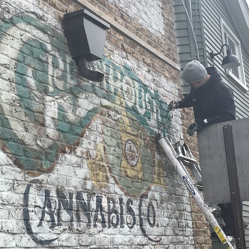 Sign painter Mark Serra adds paints a sign on the Greenhouse of Walled Lake. The store opens for recreational marijuana sales on Saturday. - Larry Gabriel