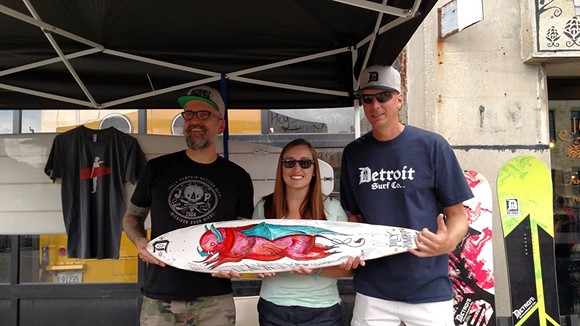 FORMAN AND DETROIT SURF CO. OWNER DAVE TUZINOWSKI POST WITH THE FINISHED LONGBOARD DESIGN AND THE RAFFLE WINNER, WHITMORE LAKE RESIDENT JULIE ANDERSON. | COURTESY OF JOLLY PUMPKIN