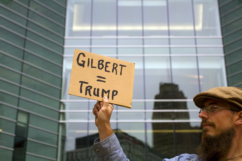 A protester holds up a sign at an August 2017 rally against a Donald Trump fundraiser in a Dan Gilbert building. - STEVE NEAVLING