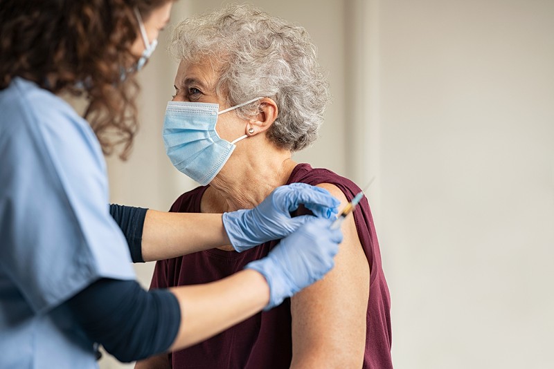 Doctor giving injection to senior woman at hospital. - SHUTTERSTOCK