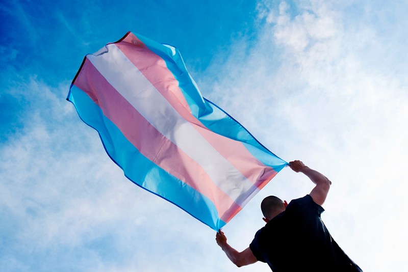 A person holding a transgender pride flag. - SHUTTERSTOCK