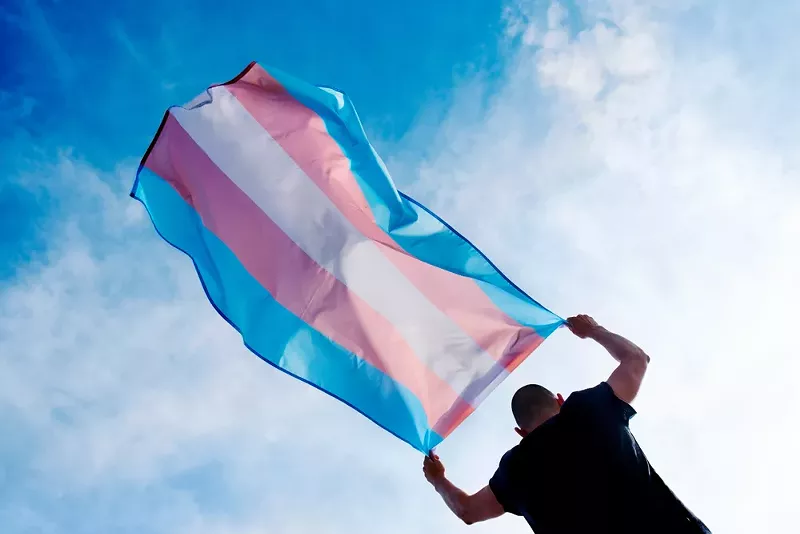 A person holding a transgender pride flag. - Shutterstock