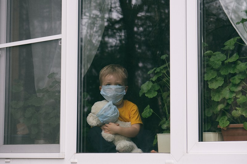 Sad child in protective medical masks looks out the window. - SHUTTERSTOCK