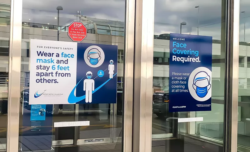 Entrance door of DTW terminal building with sign requiring masks. - gg5795 / Shutterstock.com