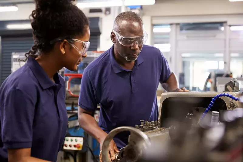 An engineer showing a teenage apprentice how to use a lathe. - Shutterstock