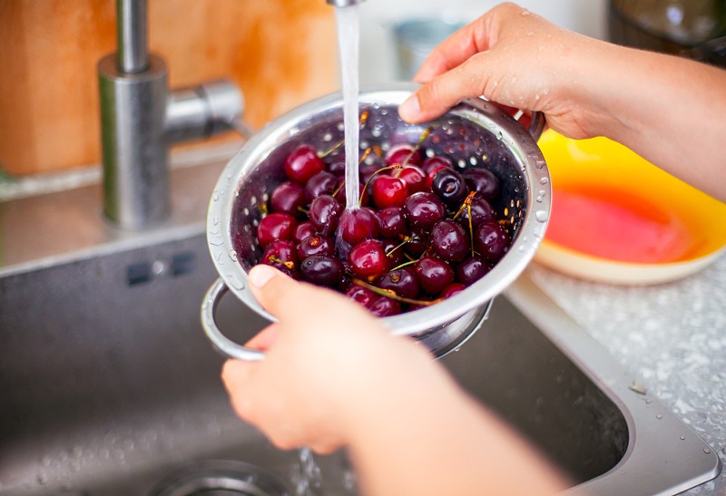 A woman washing cherries under a faucet. - Shutterstock