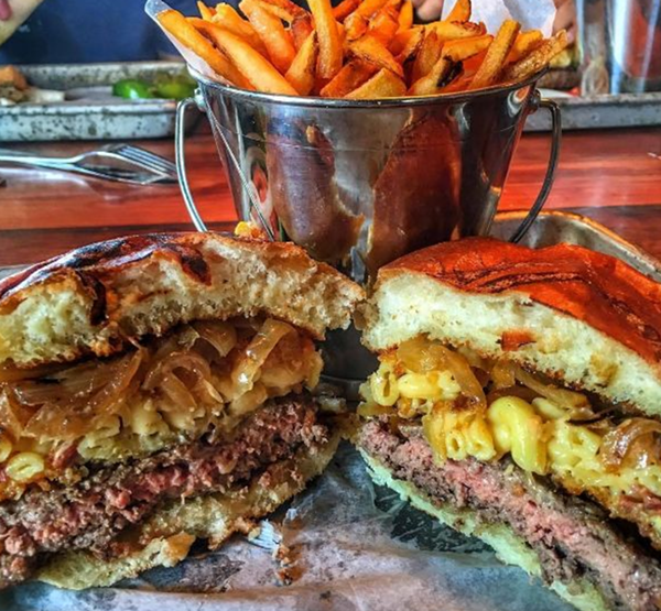 The Rusted Crow's mac and cheese burger with grilled onions, bacon, and a mac and cheese patty between the buns. - (RUSTED CROW VIA INSTAGRAM)