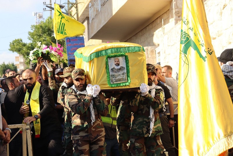 Hezbollah fighters, dressed in military uniform in Lebanon, carry a coffin wrapped in a yellow flag, mourning a fallen comrade from battles with Israel. - Shutterstock